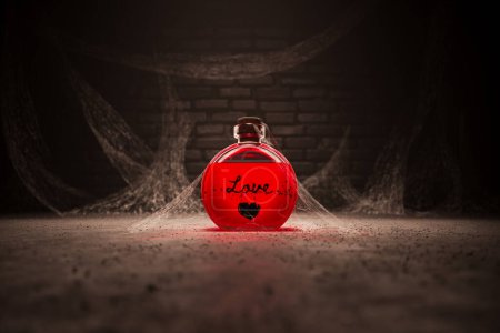 Foto de Una sola botella de poción de amor rojo que se encuentra en un antiguo sótano. Elixir potente para el romance cubierto de polvo y telas de araña. Concepto de magia, brujería, romance o farmacia. - Imagen libre de derechos