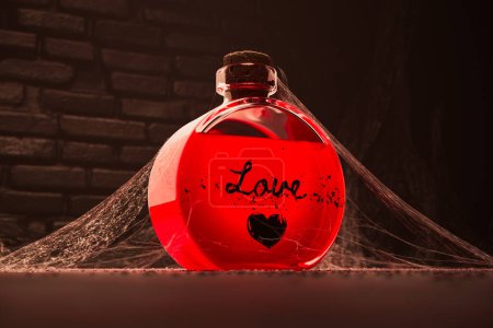 Eine einzige Flasche roten Liebestranks, die in einem alten Keller gefunden wurde. Potentes Elixier für Romantik umhüllt von Staub und Spinnennetzen. Magie, Hexerei, Romantik oder Apothekenkonzept.
