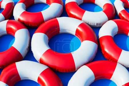 A collection of colorful inflatable rings, perfect for a day of fun in the pool. These rings are neatly arranged in red and white stripes and set against a vibrant blue background.