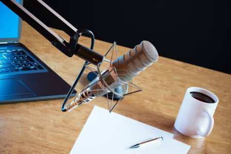 Photo for Podcast audio recording items in a climatic broadcasting home studio. Closeup on a professional microphone. Laptop, some papers and a cup of coffee on the table in the background. DOF. Journalism. - Royalty Free Image