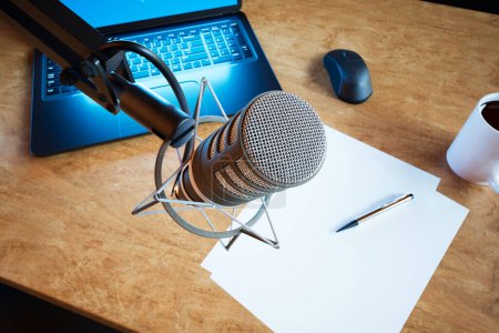 Photo for Podcast audio recording items in a climatic broadcasting home studio. Closeup on a professional microphone. Laptop, some papers and a cup of coffee on the table in the background. DOF. Journalism. - Royalty Free Image