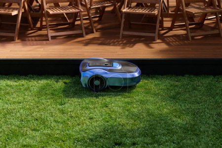 Foto de Un concepto de equipo para el hogar inteligente. Un robot de césped corta el patio mientras que una aspiradora limpia la terraza de madera en el jardín. Los electrodomésticos inalámbricos cuidan la casa. Tecnología remota moderna - Imagen libre de derechos