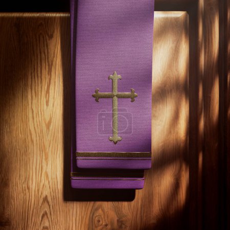 Violette Stola mit Kreuz, aufgehellt von Lichtstrahlen, die in einen Beichtstuhl fallen. Details der christlichen Kapelle. Platz in einer katholischen Kirche, um Sünden zu bekennen. Sakrament. Symbol der göttlichen Barmherzigkeit, der Vergebung