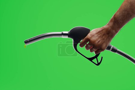 Téléchargez les photos : La dernière goutte d'essence. La main d'un homme tenant une buse de pompe à carburant sur le fond vert. Frais élevés de ravitaillement en carburant d'une voiture. Recharge de carburant pour un véhicule. De l'essence. Diesel. Le prix élevé du baril de pétrole - en image libre de droit