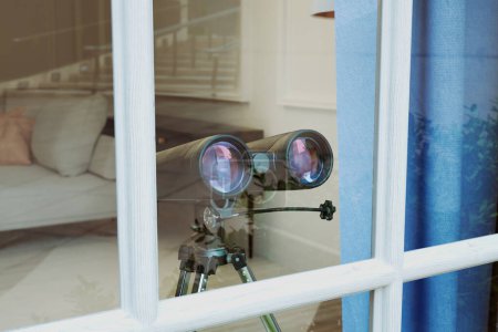 Photo for Binoculars in a window. Concept of spying technology. Spy gear. Observation equipment with field glasses ready for watching a target. Under surveillance. An atmosphere of suspense and anxiety. - Royalty Free Image
