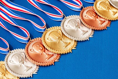 Photo for Collection of gold, silver, and bronze medals with colorful ribbons resting on a soft blue fabric background. Perfect for awards, recognition, or competition concepts. - Royalty Free Image