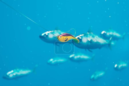 Gelbe Metallfische beißen ins blaue Wasser. Rode mit hervorragenden Ködern beim Angeln. Im Hintergrund schwimmen Fische. Hobby-Zeit. Hochseeangeln. Bunte Ausrüstung, um einen Fisch zu fangen. Wackelkandidat.