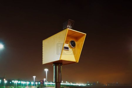 Speed camera takes photos with the flash at night. Speed control at the road. City lights in the dark background. Speed limit. Slow down. Speedometer takes measurements of cars' acceleration. Close up