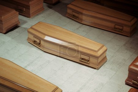 Salle de stockage remplie d'un grand nombre de cercueils en bois massif avec des poignées décoratives dorées. Un cercueil est en gros plan, prêt pour un enterrement. Industrie, affaires. Différents types et tailles de caisses.
