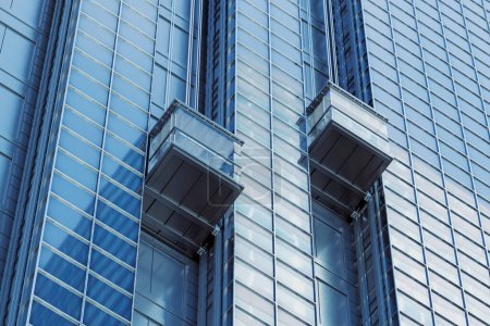 Photo for Two elevators are moving up on the side of a modern skyscraper. Blue sky reflects in the windows. The building is located in a bustling urban city, showcasing modern architecture and design - Royalty Free Image