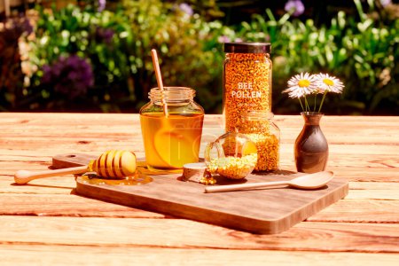 Photo for A composition with a jar of honey, dipper, wooden scoop and glass pots full of yellow bee pollen granules. Heap of flower pollen. Useful and valuable beekeeping products. Natural healthy supplement. - Royalty Free Image