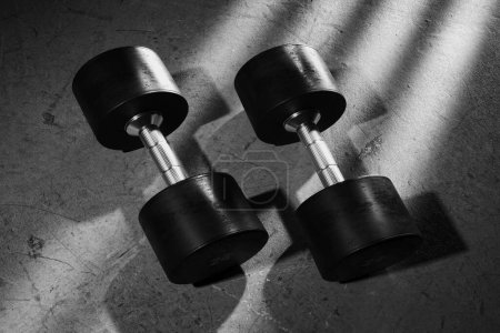 Photo for Pair Of Dumbbells isolated on a gym grey concrete floor. Modern fitness equipment for weight training, building strength, sculpting upper body muscles. Health, bodybuilding, lifting concept. - Royalty Free Image