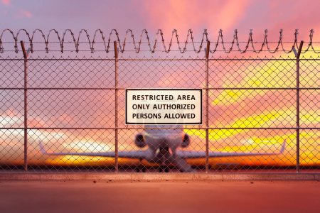 Airport fence with a restricted area signs on it. The wire fence is topped with barbed wire to provide optimal security and protection. Only authorized people are allowed to be there. Jet