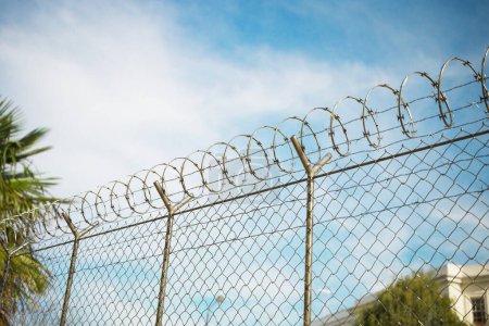Außengefängnis-Zaun aus der Perspektive eines Häftlings bei einem Spaziergang. Die Grenze der Freiheit. Der Zaun ist hoch und imposant, mit messerscharfem Draht oben, und er erstreckt sich so weit das Auge reicht