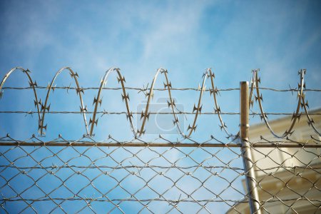 Téléchargez les photos : Une image saisit la perspective d'un prisonnier en promenade, regardant la clôture de la prison. L'image montre la dure réalité de l'incarcération et la liberté limitée. Caméra se concentre sur le fil barbelé - en image libre de droit