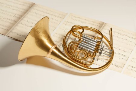 Photo for Wide shot of a French horn put on music note sheets. A brass instrument made of shiny golden tubing used by players in professional orchestras or bands. Art piece, album cover, or website header - Royalty Free Image