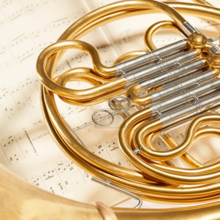 Photo for Close-up shot of a French horn put on music note sheets. A brass instrument made of shiny golden tubing used by players in professional orchestras or bands. Art piece, album cover, or website header - Royalty Free Image