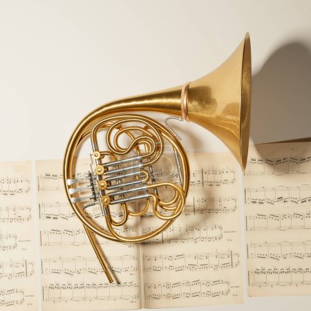 Photo for Top view shot of a French horn put on music note sheets. A brass instrument made of shiny golden tubing used by players in professional orchestras or bands. Art piece, album cover, or website header - Royalty Free Image