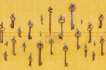 Photo for Various sizes and types of keys hanging on hooks on the yellow wall. The keys create a unique visual display that grab the attention of any viewer. Showing signs of wear and tear from years of use - Royalty Free Image
