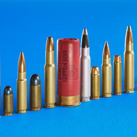 A huge row of different bullet types standing on the concrete floor. Huge variety of ammunition calibers. Handgun, carabine, automatic, shotgun, and more. Deadly combat force. Blue background