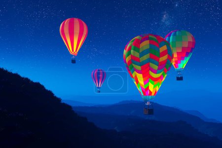 Téléchargez les photos : Des montgolfières colorées et lumineuses qui survolent les montagnes pendant une nuit. Trois grands ballons multicolores vibrants se dressant lentement contre un ciel sombre avec des étoiles. Voyage, aventure, festival. - en image libre de droit