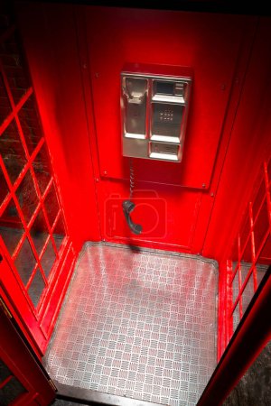 Black handset hanging in a red telephone box. Footage with British phone booth. Close up on hanging receiver above the floor. 911 emergency call was abruptly interrupted mid-call. High camera angle.