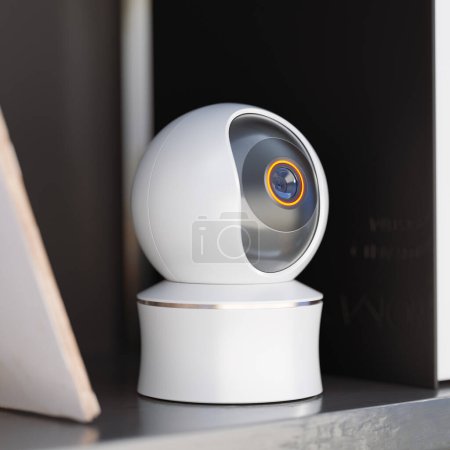 White spherical smart camera watching and recording from an office shelf. A sophisticated piece of wireless technology equipment working flawlessly. Voyeur machine gathering secret information.