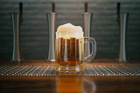 Téléchargez les photos : Tasse à bière pleine de délicieux liquide doré debout sur un comptoir de bar sous les projecteurs. Robinets de bière et mur de briques en arrière-plan. La boisson alcoolisée froide provoque la condensation de l'eau sur une surface en verre. - en image libre de droit