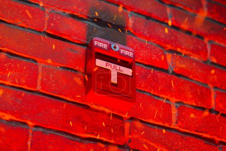 Téléchargez les photos : Alarme incendie rouge tirée lors d'un incendie croissant. Braises chaudes et orange émises par le feu se déplaçant vers le haut d'une manière chaotique. Vieux mur de briques en arrière-plan illuminé par des couleurs de feu chaud. - en image libre de droit