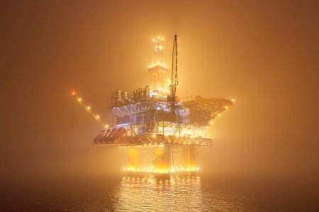 Photo for Big oil rig working on an open ocean during a foggy night. Countless lights illuminate the mist and create a reflection in the water waves. Symbol of natural environment degradation and pollution. - Royalty Free Image