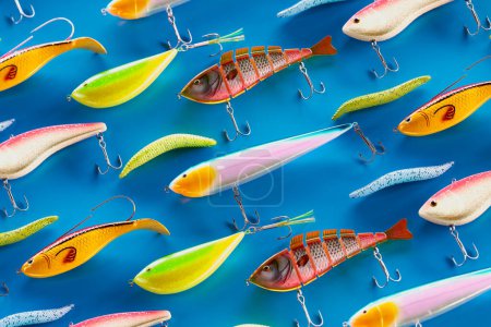 Foto de Una fila de diversas picaduras de peces de colores. Conjunto de señuelos multicolores y anzuelos para el hobby de la pesca. Se encarga de atrapar un pez. Equipo de pesca en un fondo azul. Wobblers. entusiastas de la pesca - Imagen libre de derechos