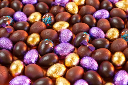Téléchargez les photos : Collection de petits œufs de Pâques au lait et chocolat noir. Chaque oeuf est décoré de façon unique, avec certains enveloppés dans de l'or brillant et du papier d'aluminium violet - un régal parfait pour les joyeuses célébrations de Pâques. - en image libre de droit