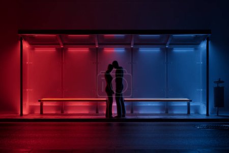 Téléchargez les photos : Captivée par une étreinte, la silhouette d'un couple se fond sous le scintillement néon d'un arrêt de bus urbain, un moment privé d'amour juxtaposé au fond urbain nocturne. - en image libre de droit