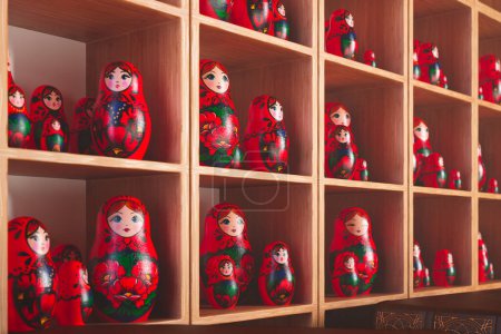 Una exposición elaborada de muñecas Matryoshka, cada una pintada con diseños populares tradicionales rusos, alinea los estantes de una pintoresca tienda, presentando un tapiz de arte cultural y colores vibrantes..
