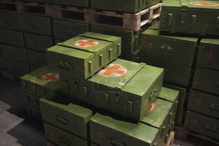 Precisely arranged stack of green military-grade medical crates adorned with red cross symbols, stored securely for swift response to potential field emergencies or disaster relief missions.