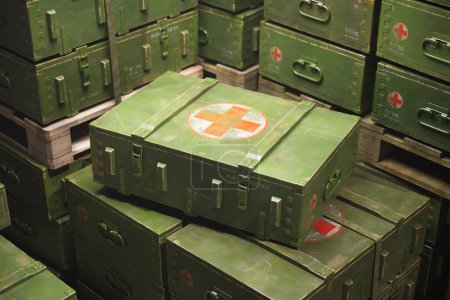 Nahaufnahme gestapelter olivgrüner militärischer medizinischer Kisten mit roten Kreuzen, die die Bereitschaft zur medizinischen Notfallversorgung und die effiziente Lagerung medizinischer Hilfsgüter für Außeneinsätze symbolisieren.