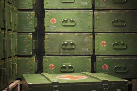 Neatly organized military medical supplies, featuring prominently displayed red crosses on green boxes, within a secure, dimly lit military storage facility.