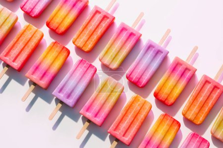 Photo for An eye-catching display of mixed fruit-flavored ice pops lined up on a vivid pink background, highlighting the delightful contrast and tempting summer treat appeal. - Royalty Free Image