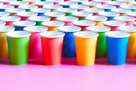 This eye-catching display features a geometric array of bright, multicolored disposable paper cups against a striking pink background, symbolizing modern sustainability.