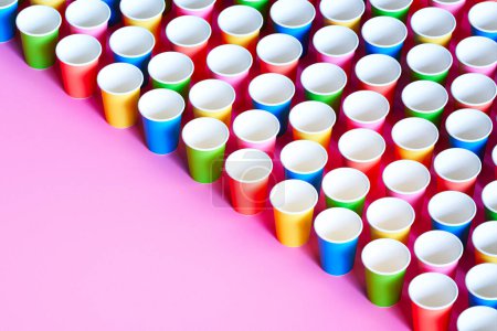 Affichage frappant de tasses jetables colorées disposées en diagonale sur un fond rose pastel, mettant en évidence les thèmes de l'essentiel de la fête et des jetables éco-conscients.