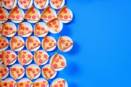 Foto de Esta llamativa imagen muestra una variedad de rebanadas de pizza de pepperoni colocadas en platos blancos, formando un patrón vibrante y de aspecto delicioso sobre un fondo azul vivo.. - Imagen libre de derechos