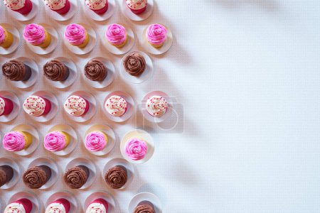 Téléchargez les photos : Une délicieuse collection de cupcakes assortis, aux riches saveurs de chocolat et de vanille crémeuse ornée de glaçage rose et marron, présentés élégamment sur une surface blanche immaculée. - en image libre de droit
