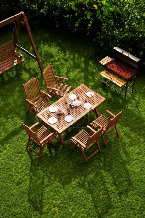 Photo for Outdoor gatherings with this serene aerial shot of a backyard barbecue area, showcasing a rustic dining table, swinging chair, lush greenery, and a grill artfully arranged for a family meal. - Royalty Free Image