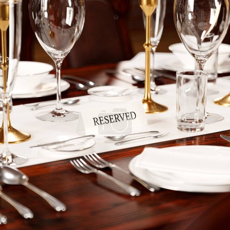 Photo for A meticulously arranged dining table with polished cutlery, crystal glassware, and an elegant "RESERVED" sign indicates an exclusive gastronomic event. - Royalty Free Image