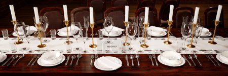 Photo for This image exhibits a luxurious table setup for a sophisticated dining affair, featuring gleaming silverware, elegant stemware, and a noticeable reserved sign amid a table arrangement draped in linen. - Royalty Free Image