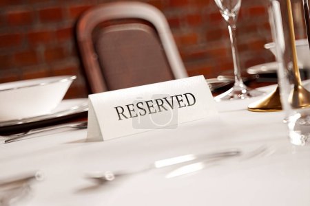 Téléchargez les photos : Une table finement aménagée avec une plaque "RÉSERVÉE" dans un restaurant haut de gamme, mettant en valeur une atmosphère luxueuse avec une vaisselle immaculée et une ambiance invitante pour un événement spécial ou un dîner. - en image libre de droit