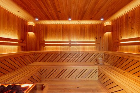 Foto de Lujosa sauna moderna con elegantes bancos de madera, paredes, calentador térmico e iluminación relajante, ideal para relajarse y disfrutar de la salud en un entorno sereno. - Imagen libre de derechos