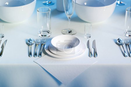 Foto de Una mesa de comedor inmaculadamente arreglada que muestra platos blancos nítidos, cubiertos de plata relucientes y vidrios de cristal lustrosos contra un mantel azul marino.. - Imagen libre de derechos