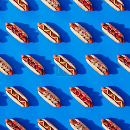 Ein sorgfältig arrangiertes, nahtloses Muster köstlicher Hot Dogs mit Senf und Ketchup, anschaulich über einem leuchtend blauen Hintergrund ausgebreitet für einen eindrucksvollen visuellen Effekt.