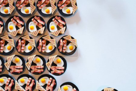 Téléchargez les photos : Une configuration esthétiquement agréable de assiettes de petit déjeuner alignées dans un motif symétrique, mettant en valeur des œufs parfaitement cuits côte à côte ensoleillés associés à du bacon croustillant, présentés sur un fond blanc immaculé. - en image libre de droit